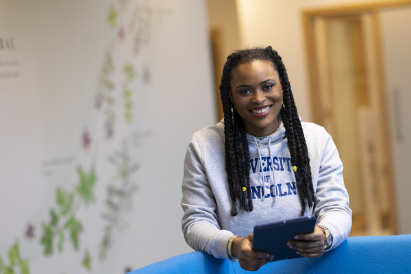 A student holds a tablet while smiling at the camera