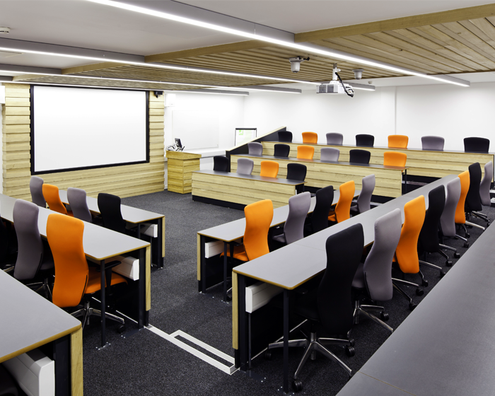 An empty working space with multiple chairs, desks, a projection screen and a computer