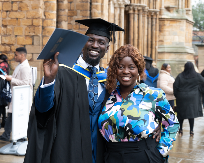 Graduate and guest smiling at graduation in front of Lincoln Cathedral
