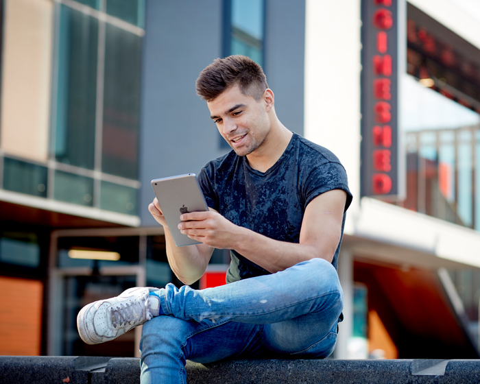 A male student sat outside the Engine Shed, using an iPad