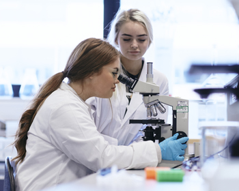 Two female students in the laboratory looking through a microscope