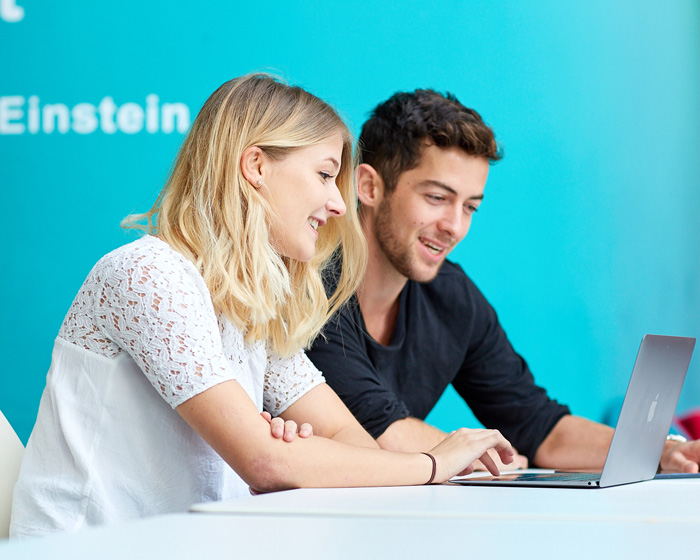 Two students discussing work in front of a laptop