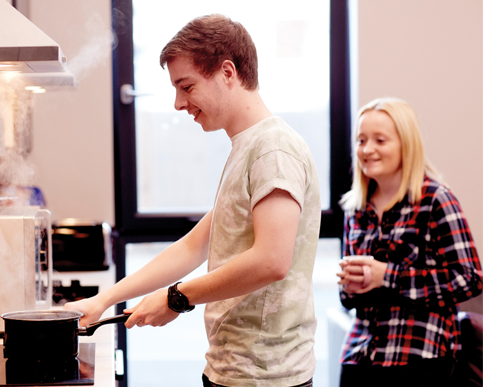 A male student cooking while a female student looks on