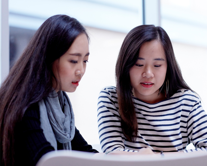 Two female students sat at a desk with their attention focused downwards