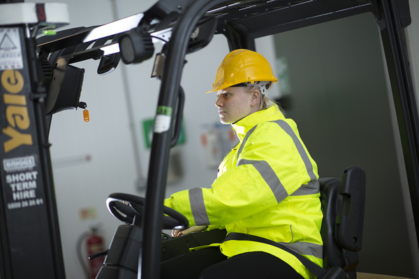 A person in a high vis jacket driving a forklift