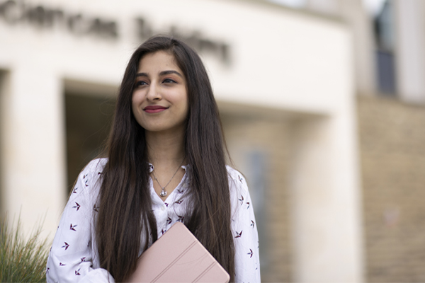 A student holding a laptop and standing in front of the medical school building