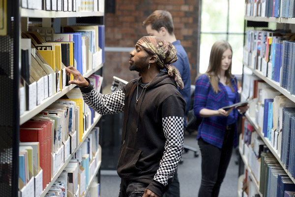 Three students looking at books in the library